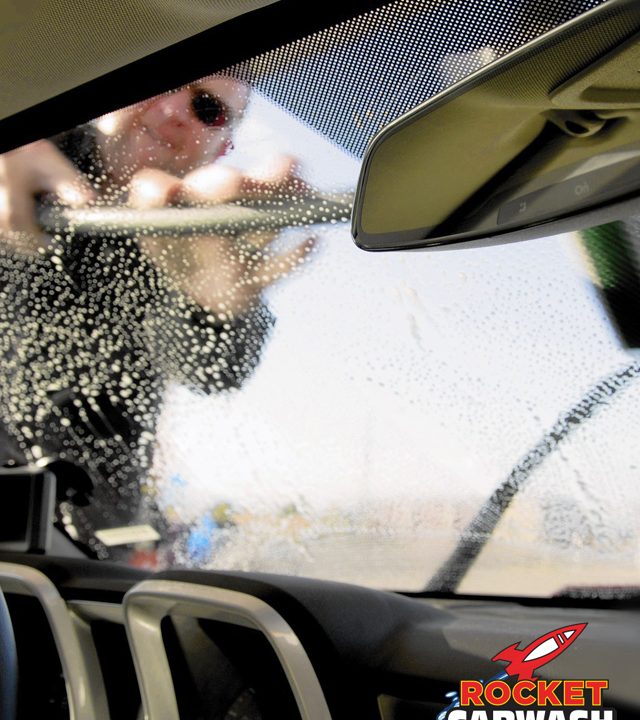 a man cleaning his car windshield off with a squeegee