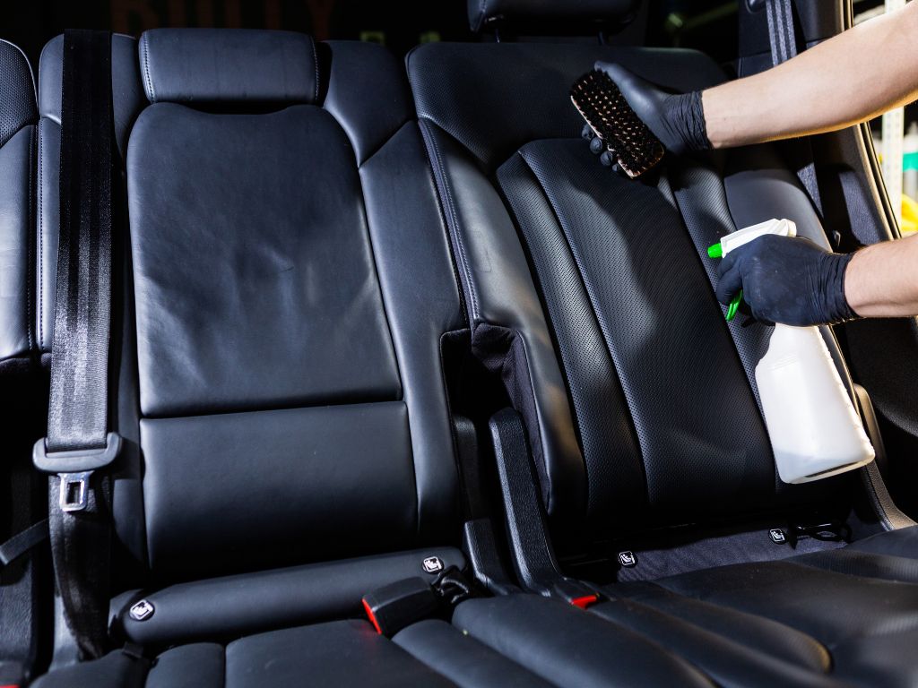car's leather interior - professional detailer using cleaning solution on black leather seats